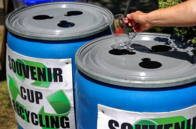 Recycling barrels with a hand dropping a plastic mug. 