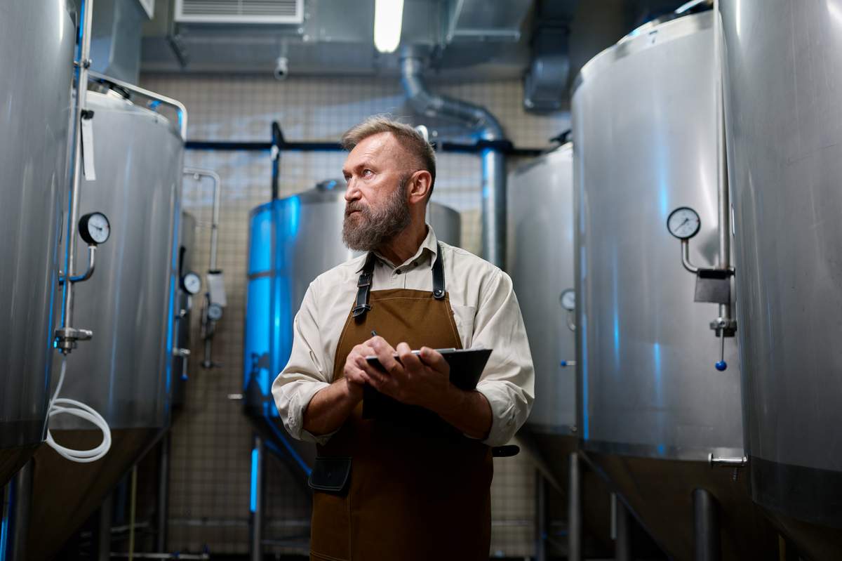 brewery worker employee checking tanks with clipboard